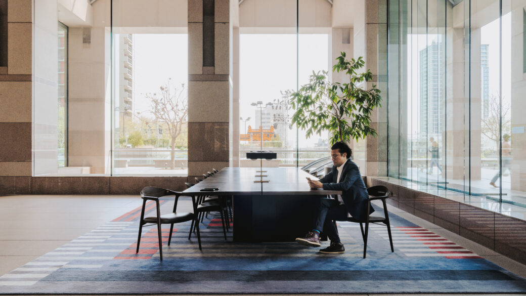 Photo of a man sitting at a large shared work desk in the lobby of 1 Cal Plaza