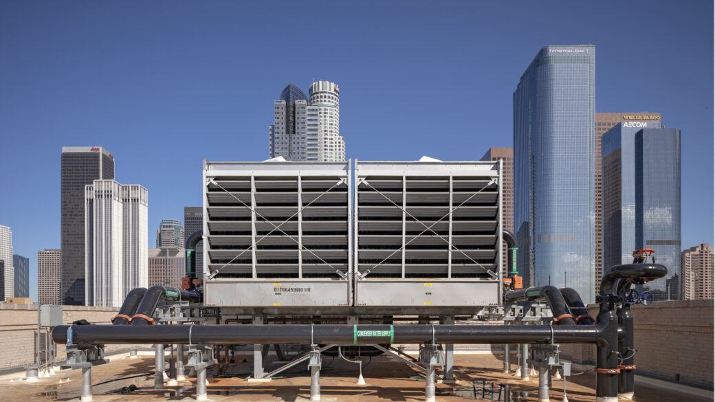 A large commercial air conditioning unit on the rooftop of The Trust Building with the Downtown Los Angeles Skyline in the background.