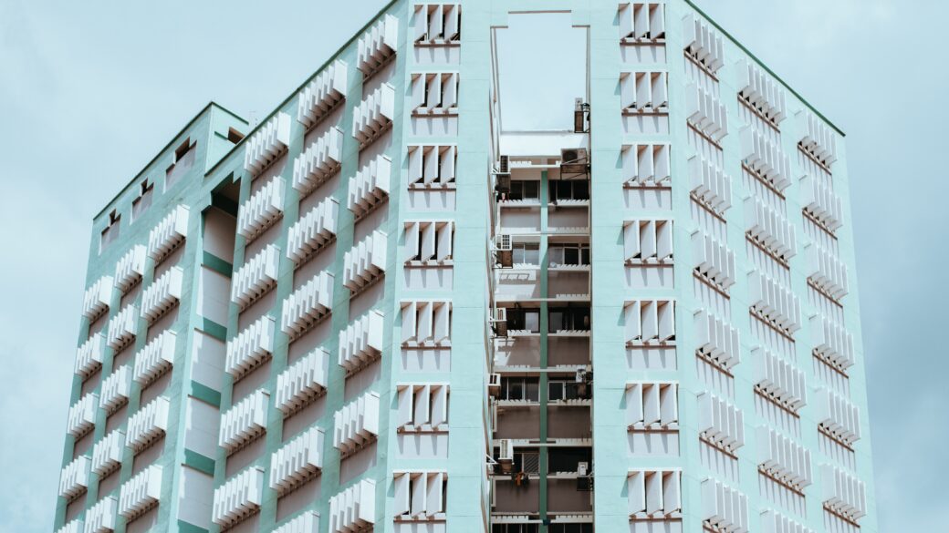 Photo of turquoise apartment building with the blue sky in behind it.