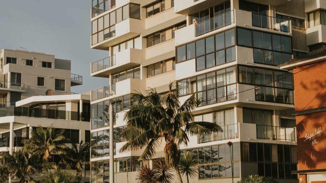 Exterior photo of a multi-family apartment building in Los Angeles with palm trees and tropical plants in front.