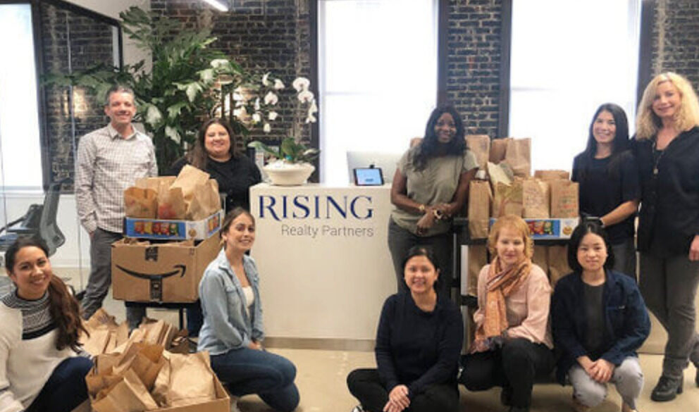 A group of Rising Realty Partners team members standing in the office lobby with meals for a food drive