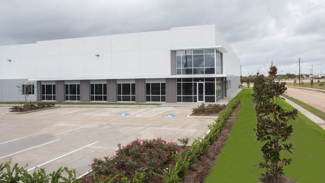 The cloudy sky above an industrial park in Southwest Houston envelopes a large, modern building with numerous windows.