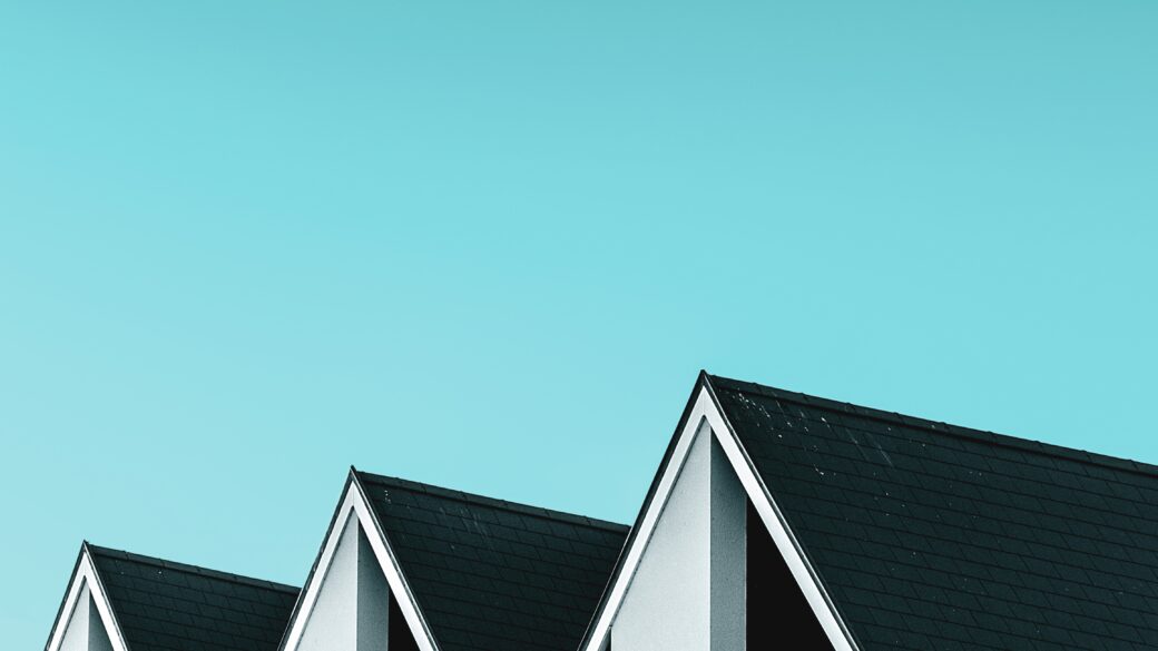 A row of elegant grey/green homes stands tall in a residential district, surrounded by a vast blue sky.