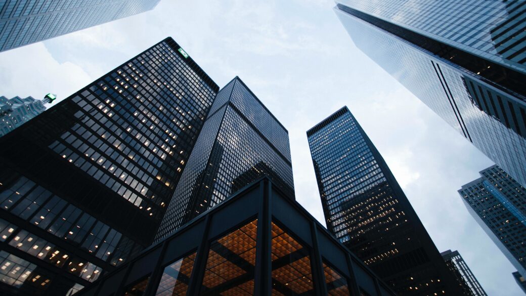 A ground up view looking up at the modern skyline of a metropolitan city filled with glass skyscrapers and the gray blue sky behind them.