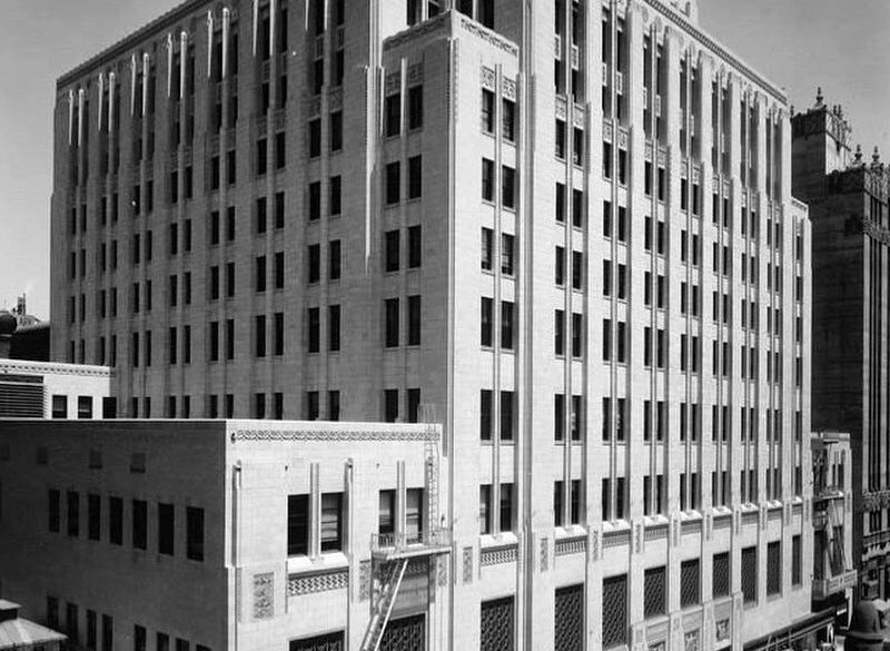 A historical black and white exterior photo of The Trust Building with vintage cars parked on the street out front.