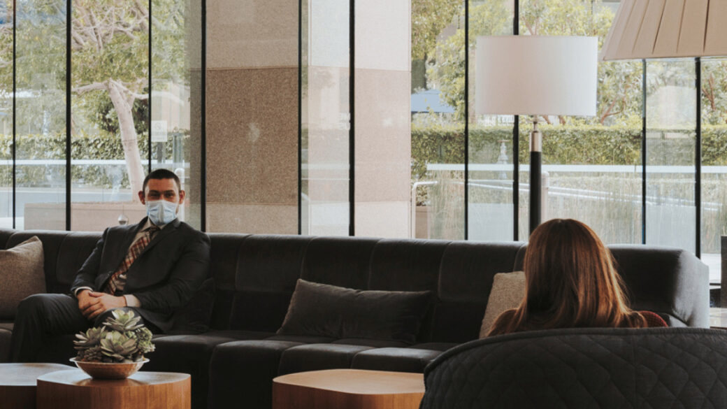 Two people wearing COVID masks sitting in the lobby of a newly reopened office building