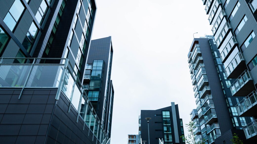 Photo of a staircase running up to a group of tall, dark multi-family apartment building with a white sky behind them.